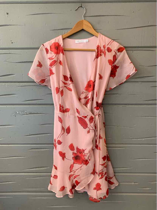 Pink floral wrap dress with short flutter sleeves and ruffled hem on wooden hanger.