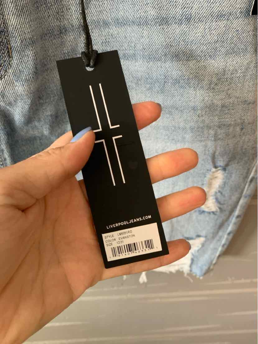 Black rectangular clothing tag with white minimalist logo and barcode held over light blue denim fabric.