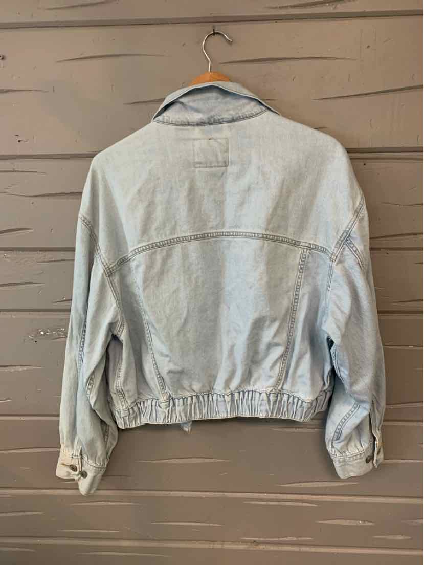 Light wash denim jacket with elastic waist and buttoned cuffs hanging on wooden hanger.