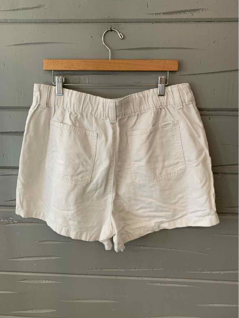 White denim shorts size 14 with front pockets and belt loops hanging on wooden hanger against gray wall.