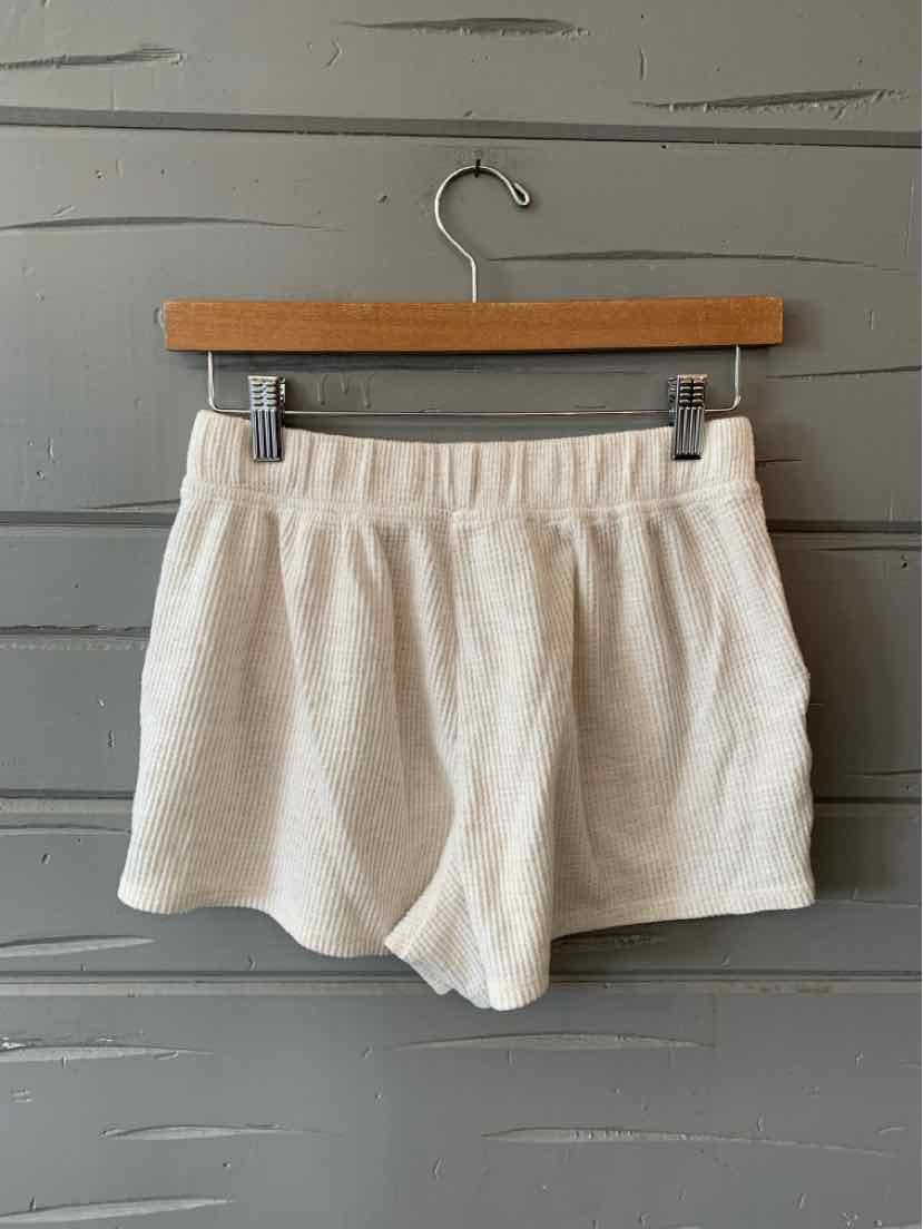 Soft white knit shorts with elastic waistband and relaxed fit hanging on wooden hanger against gray wooden background.