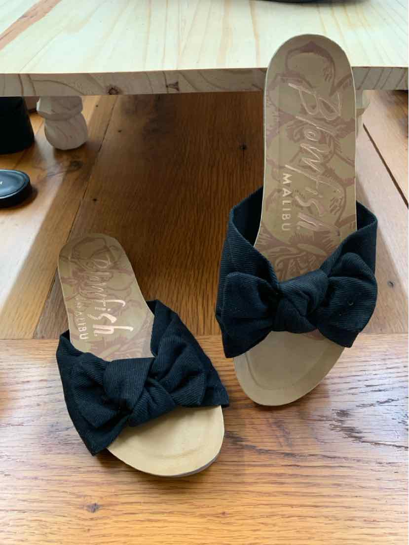 Black slide sandals with large fabric bow on top, beige footbed, and open toe design.