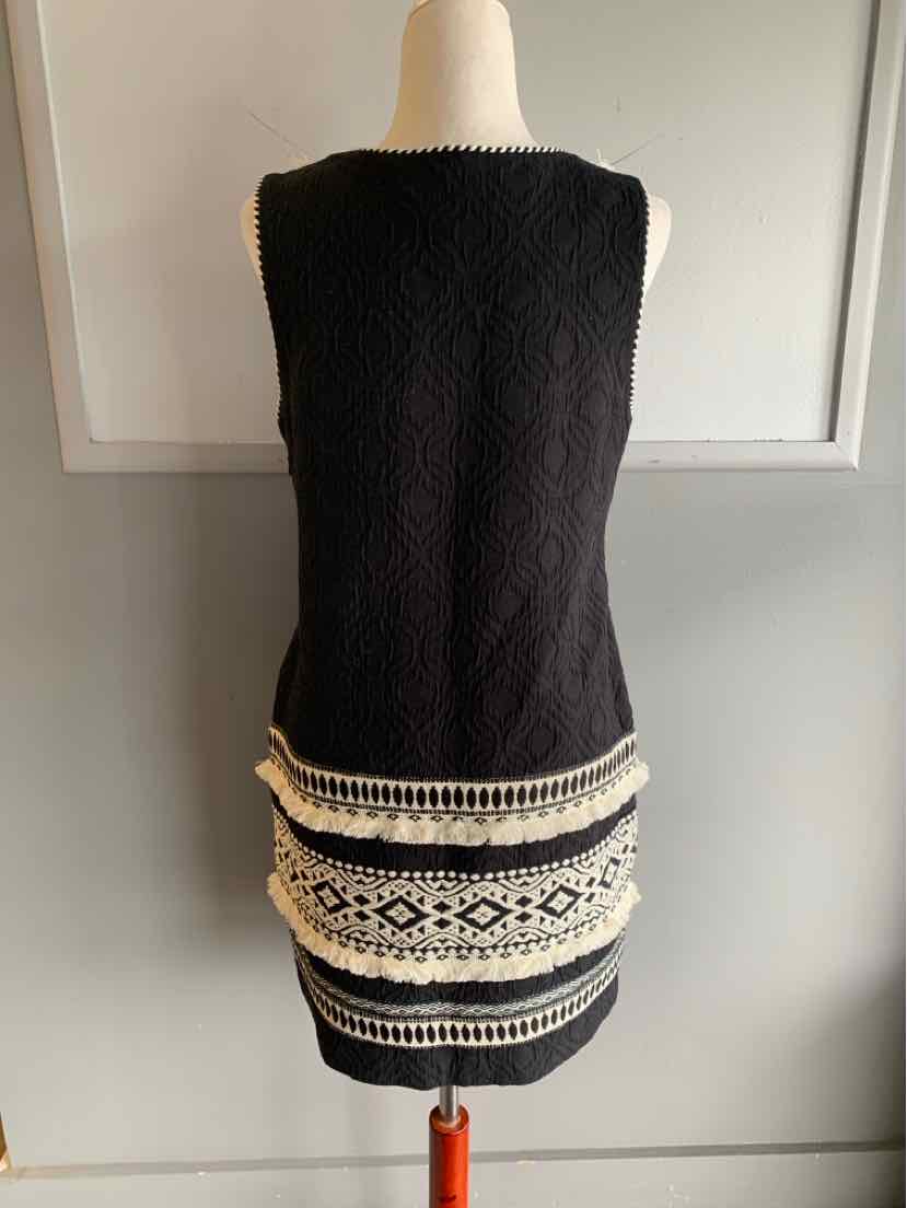 Black sleeveless knit dress with white geometric embroidered patterns near hem, fitted silhouette, short length.