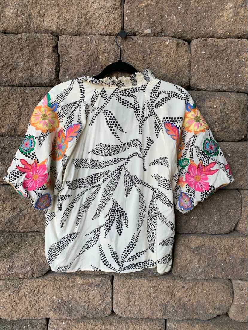 White short-sleeve shirt with black leaf print and vibrant pink, orange floral sleeves.