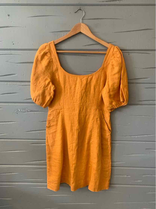 Tan linen mini dress with puffed elbow-length sleeves and scoop neckline hanging on wooden hanger.