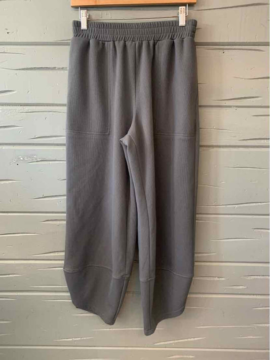 Gray casual pants with elastic waistband and wide legs hanging on wooden hanger against light gray wooden wall.