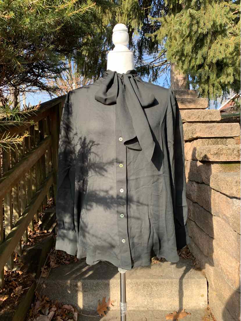 Black long-sleeve blouse with a front tie neck and button-down closure on a mannequin outdoors.