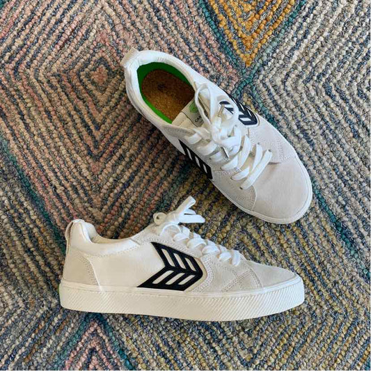 White low-top sneaker with black chevron logo on side, white laces, and textured sole.