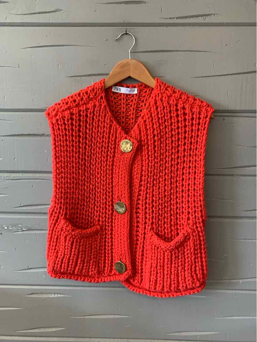 Red chunky knit sleeveless cardigan with large wooden buttons and front pockets.