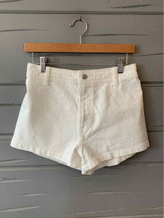 White high-waist denim shorts with front button and zipper closure, two front pockets, and cuffed hems on a wooden hanger.