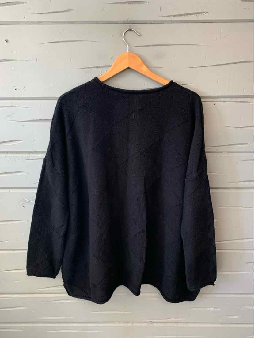 Black oversized knit sweater with long sleeves and a rounded neckline, hanging on a wooden hanger.