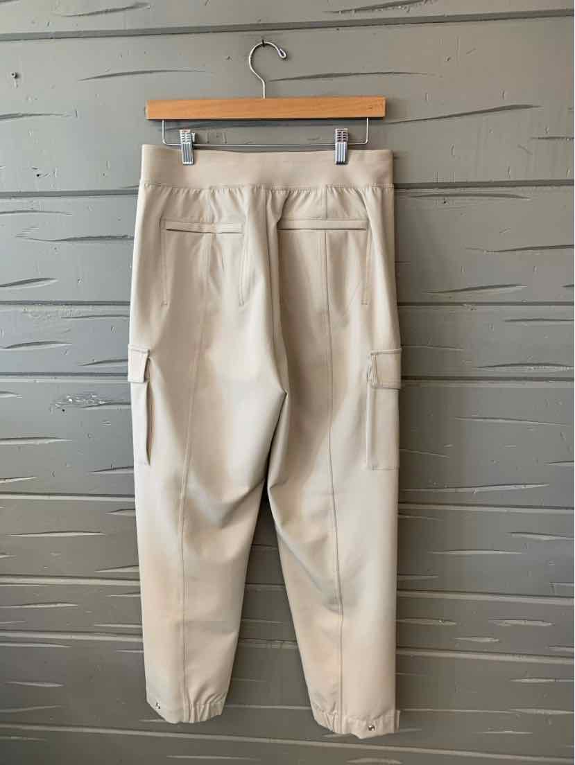 Beige tapered pants with elastic cuffs, rear welt pockets, and side cargo pocket hanging on wooden hanger.