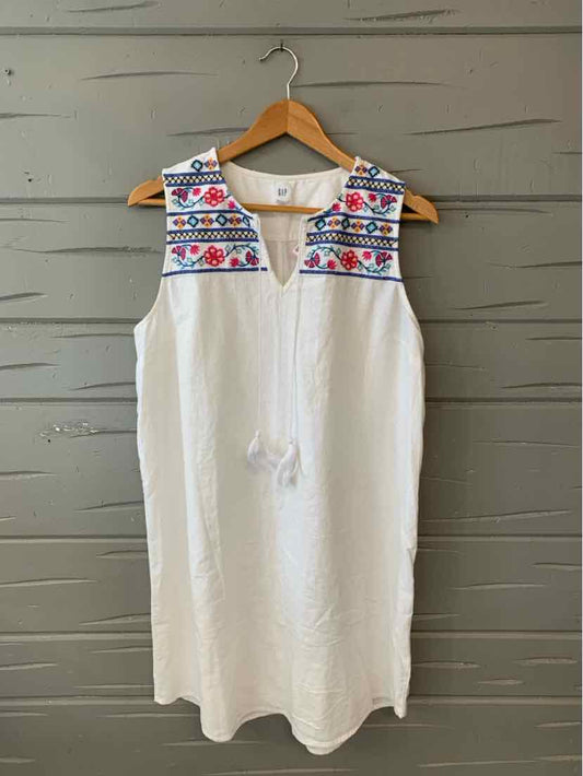 White sleeveless dress with colorful embroidered yoke and tassel tie neckline on wooden hanger.