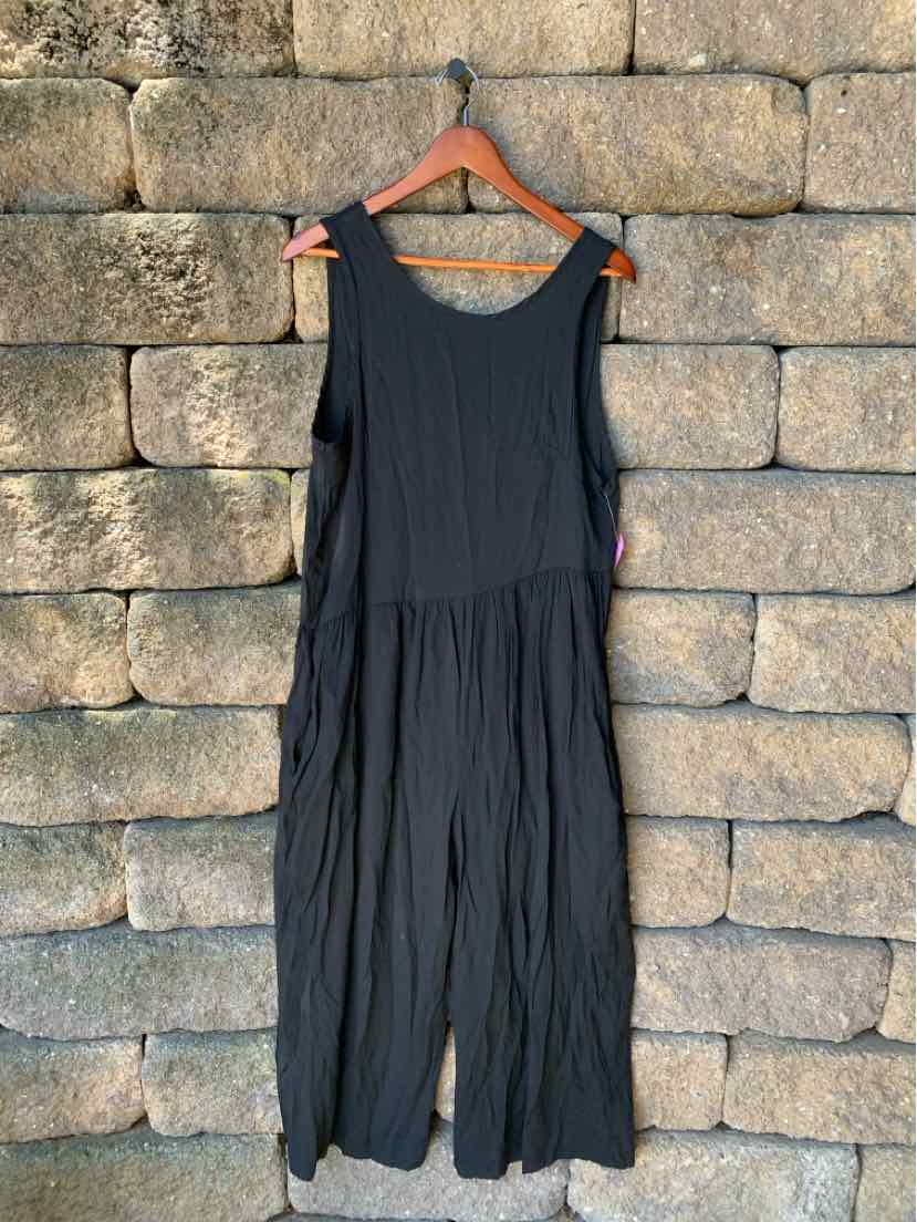Black sleeveless romper with wide legs and a scoop neckline hanging on wooden hanger.