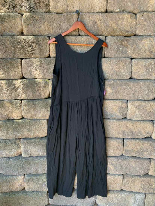 Black sleeveless romper with wide legs and a scoop neckline hanging on wooden hanger.