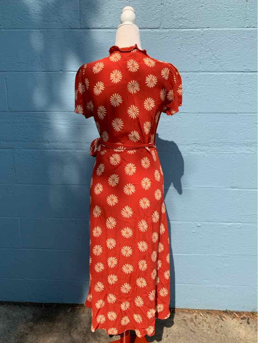 Red midi dress with white floral print, short sleeves, and a waist tie belt on a mannequin against a blue wall.