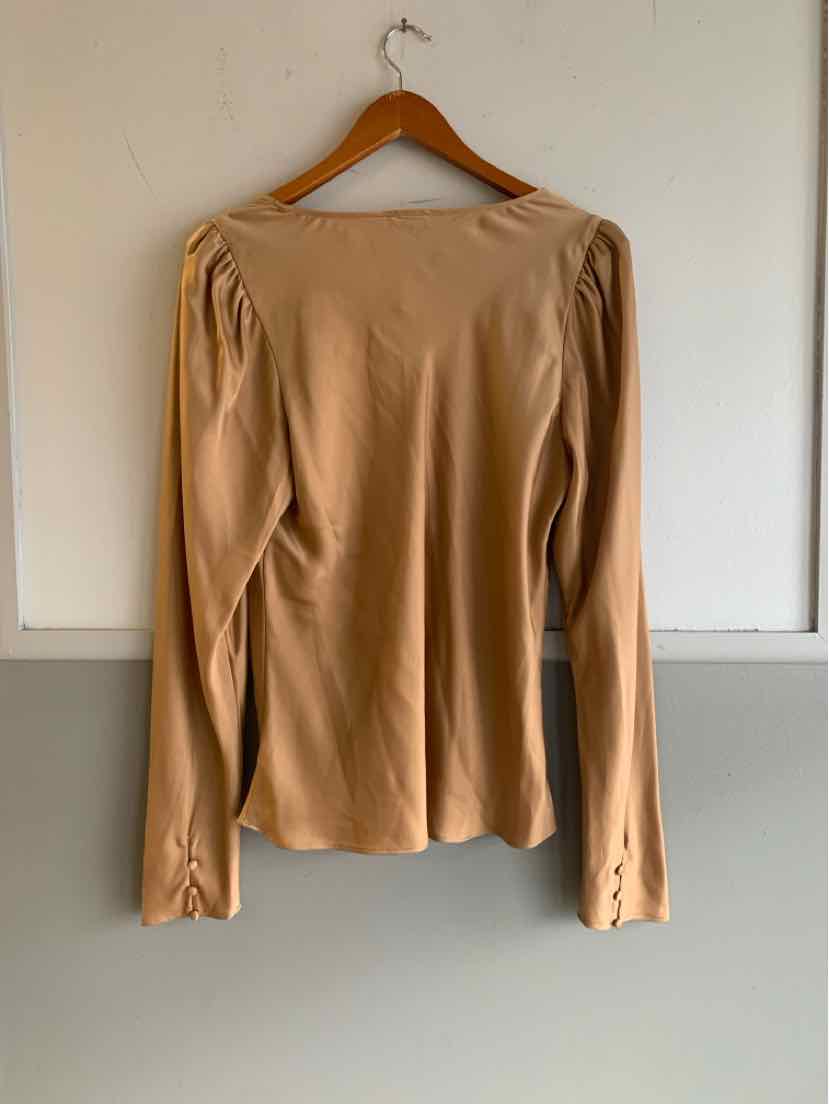 Tan long-sleeve top with puffed shoulders hanging on wooden hanger against white wall.