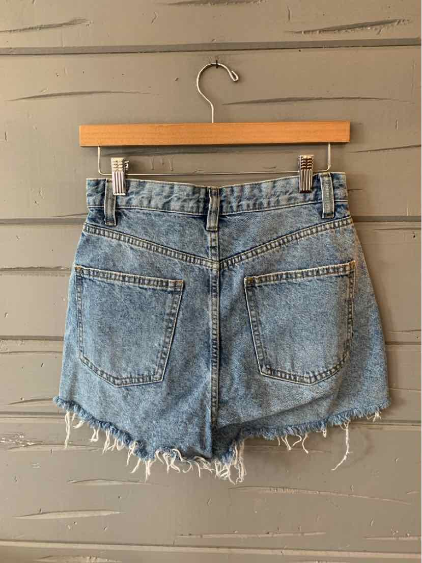 Light blue denim shorts with frayed hems and two back pockets hanging on wooden hanger against gray wall.