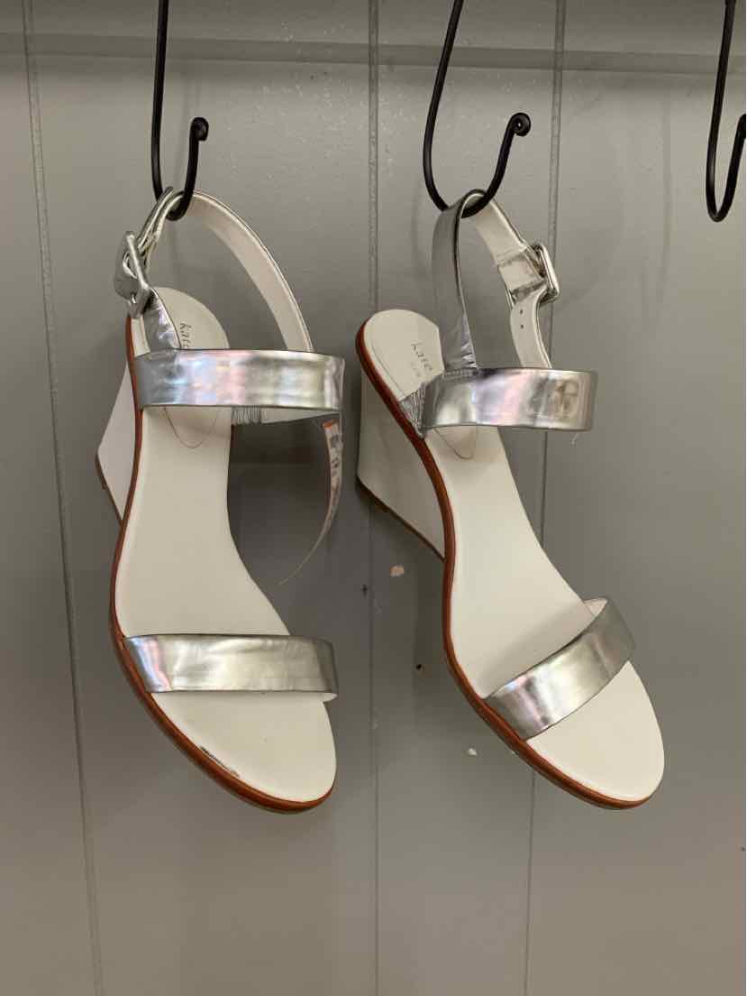 White open-toe sandal with shiny silver ankle and toe straps, flat sole, and adjustable buckle.