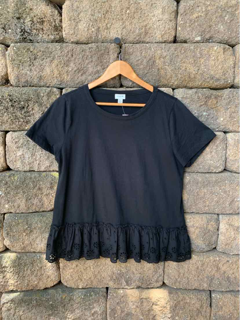 Black short-sleeve blouse with round neckline and ruffled hem detail hanging on wooden hanger.