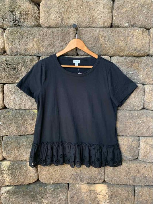 Black short-sleeve blouse with round neckline and ruffled hem detail hanging on wooden hanger.