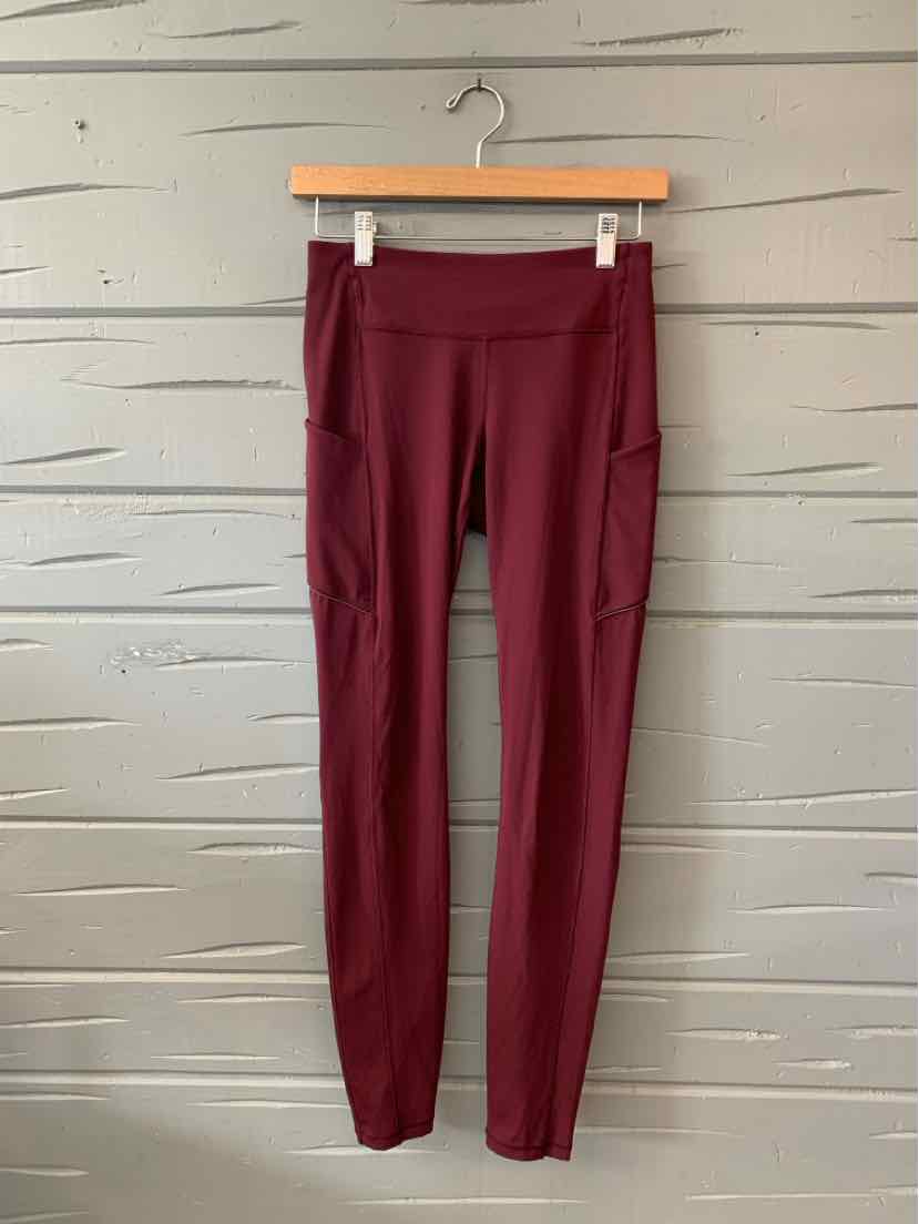 Burgundy high-waist leggings with side pockets and a slim fit hanging on a wooden hanger.