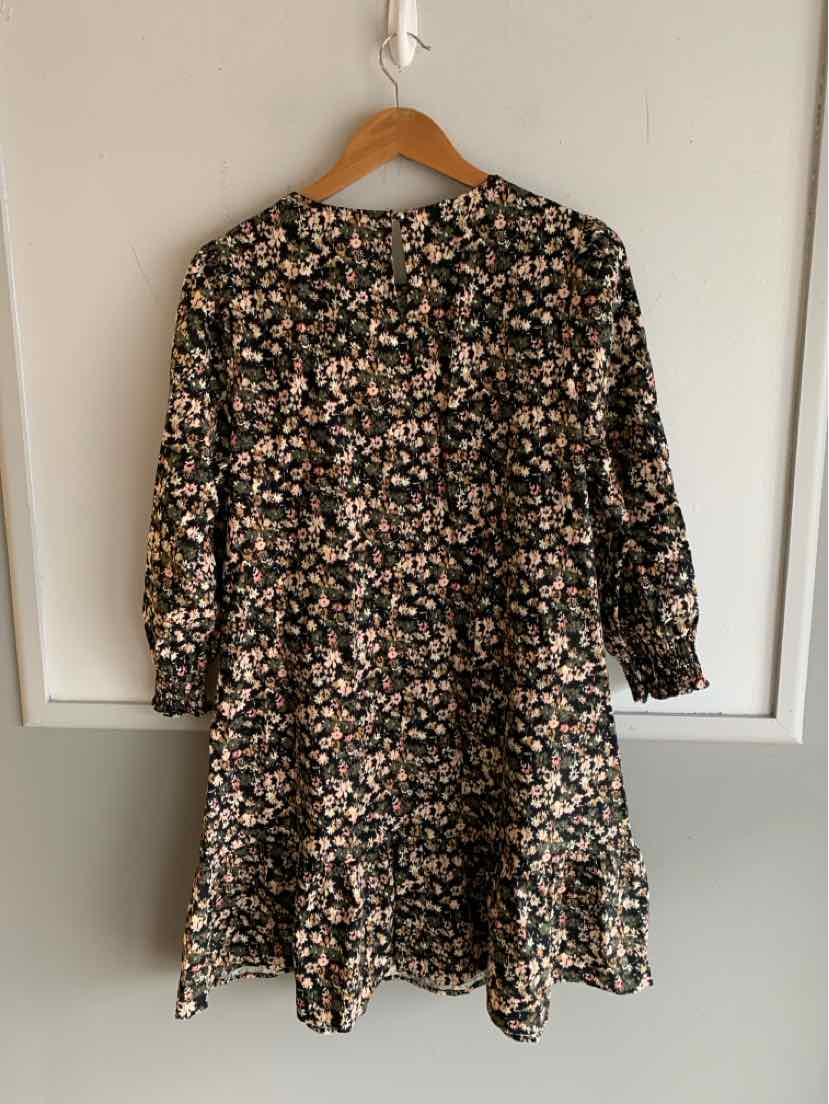 Black long-sleeve floral dress with ruffled hem and relaxed fit hanging on wooden hanger.