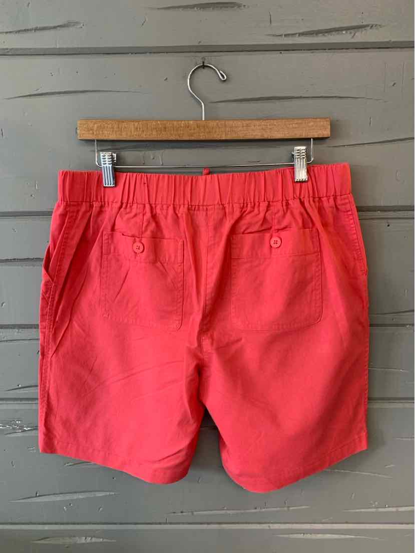 Coral pink shorts with elastic waistband and front pockets hanging on wooden hanger against gray background.