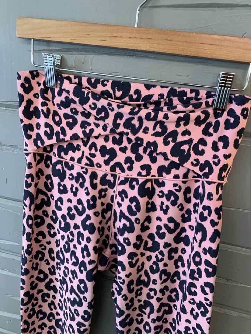Pink leopard print leggings with high waistband hanging on wooden hanger against gray wall.