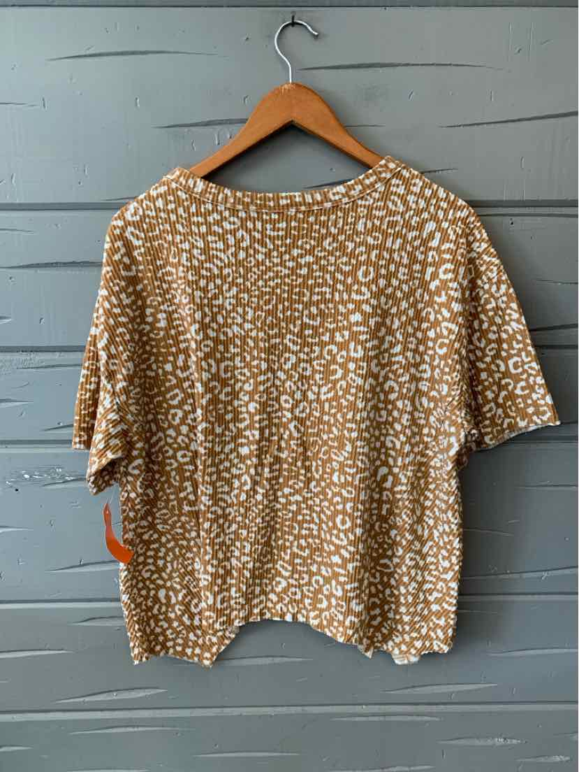 Beige short-sleeve blouse with white cheetah print and loose fit on wooden hanger.