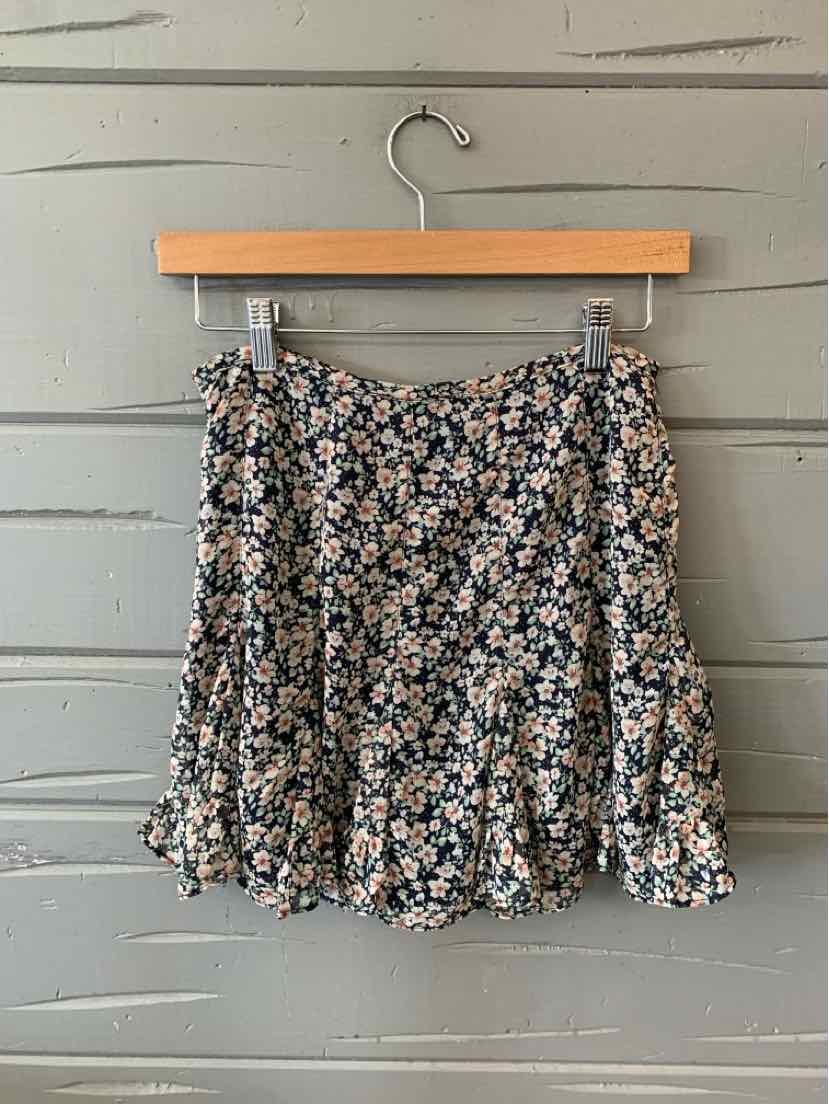Black floral mini skirt with white and pink flowers, ruffled hem, lightweight fabric.