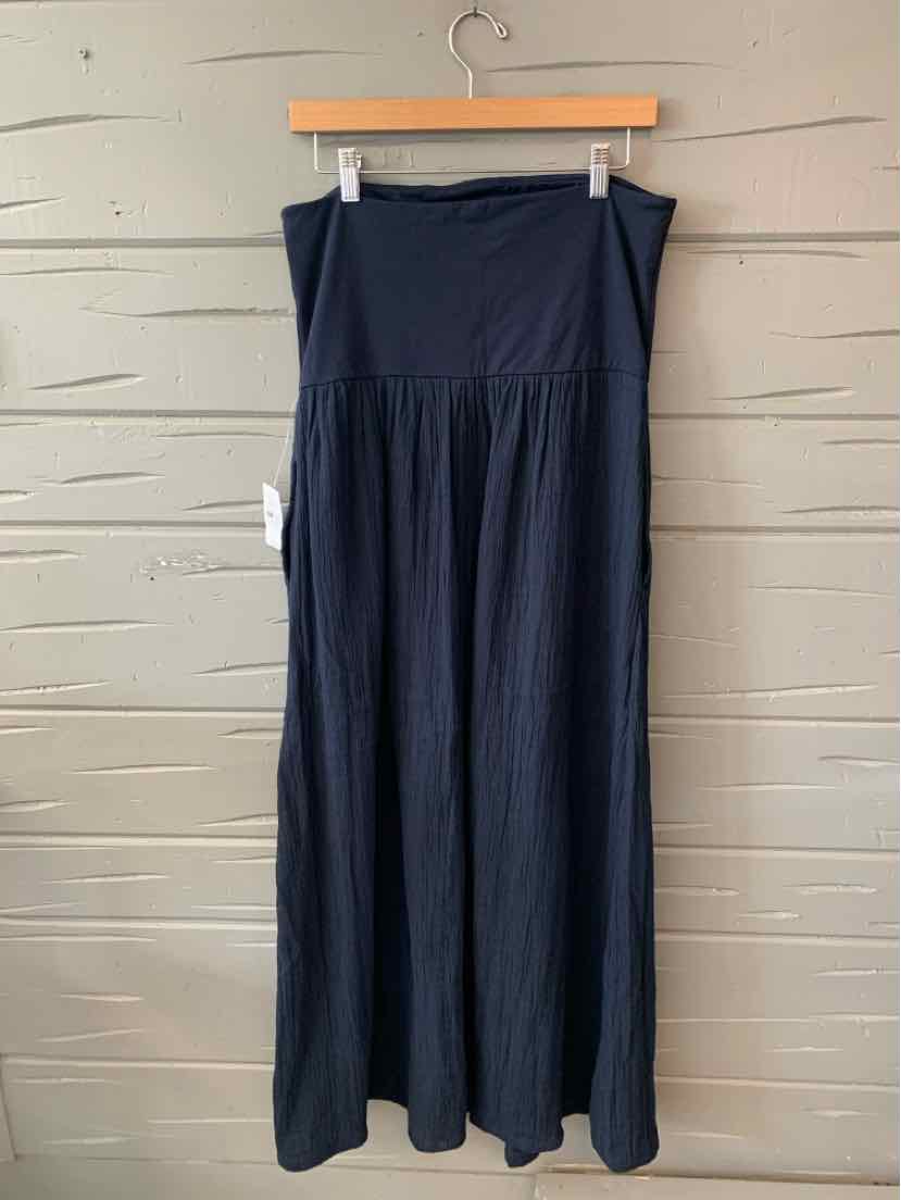 Black maxi skirt with high waistband and flowing fabric hanging on wooden hanger against beige wall.