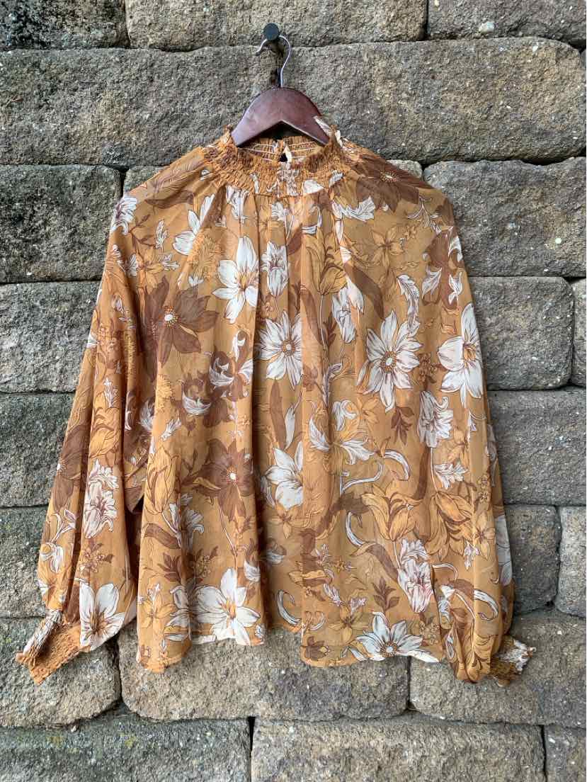 Brown floral long-sleeve blouse with high collar and gathered detailing on wooden hanger.