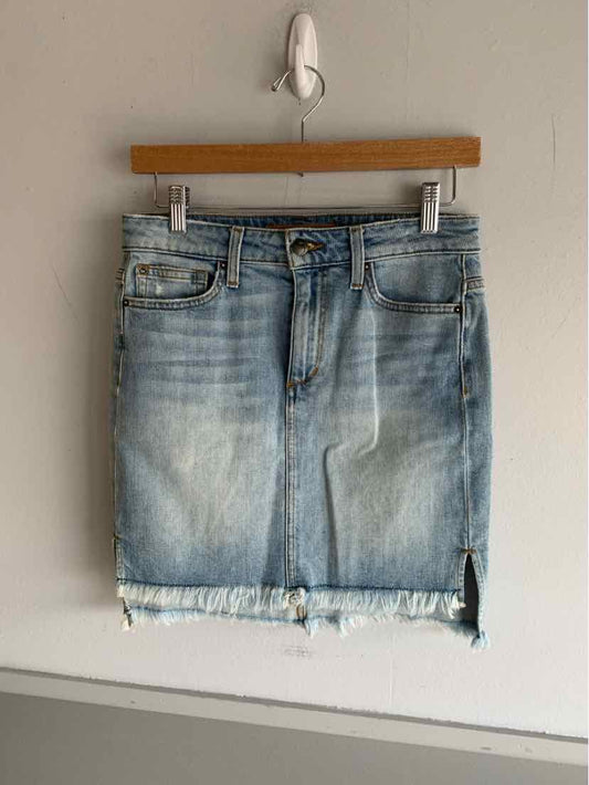 Light blue denim mini skirt with front pockets and frayed hem hanging on wooden hanger.