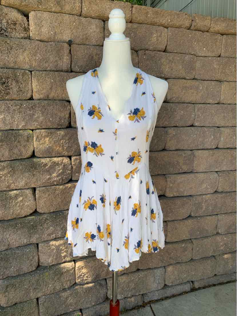 White sleeveless floral romper with yellow and blue flower print, V-neck, and flowy skirt hem.