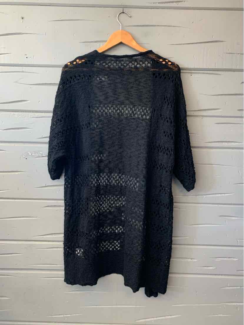 Black open-knit long cardigan with three-quarter sleeves and a scalloped hem, hanging on a wooden hanger.
