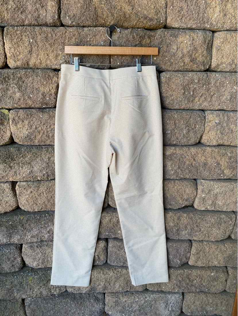 Tan straight-leg pants with back pockets hanging against a stone wall backdrop.