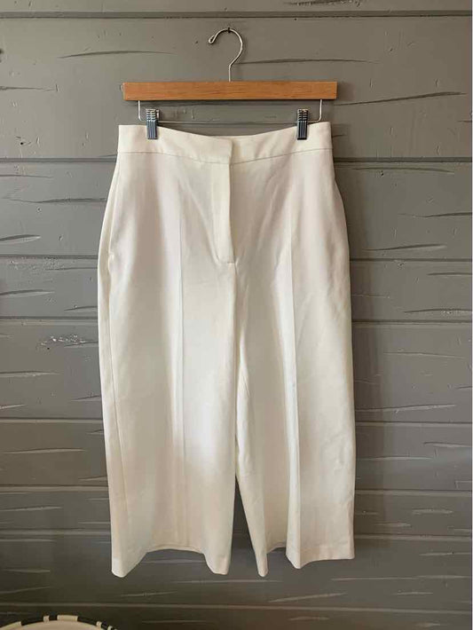 White high-waist wide-leg pants with front pleats and zipper closure on wooden hanger.