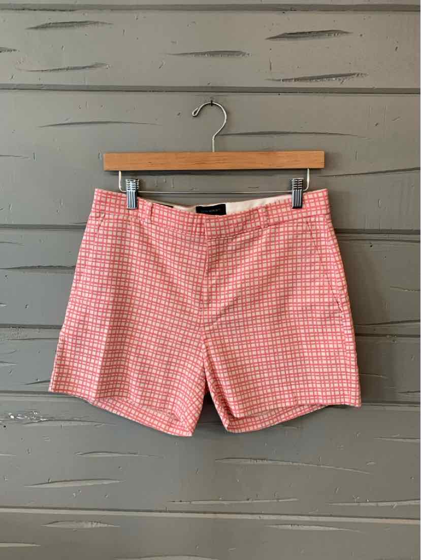 Pink and white checkered cotton shorts with front pockets and zipper closure hanging on wooden hanger.