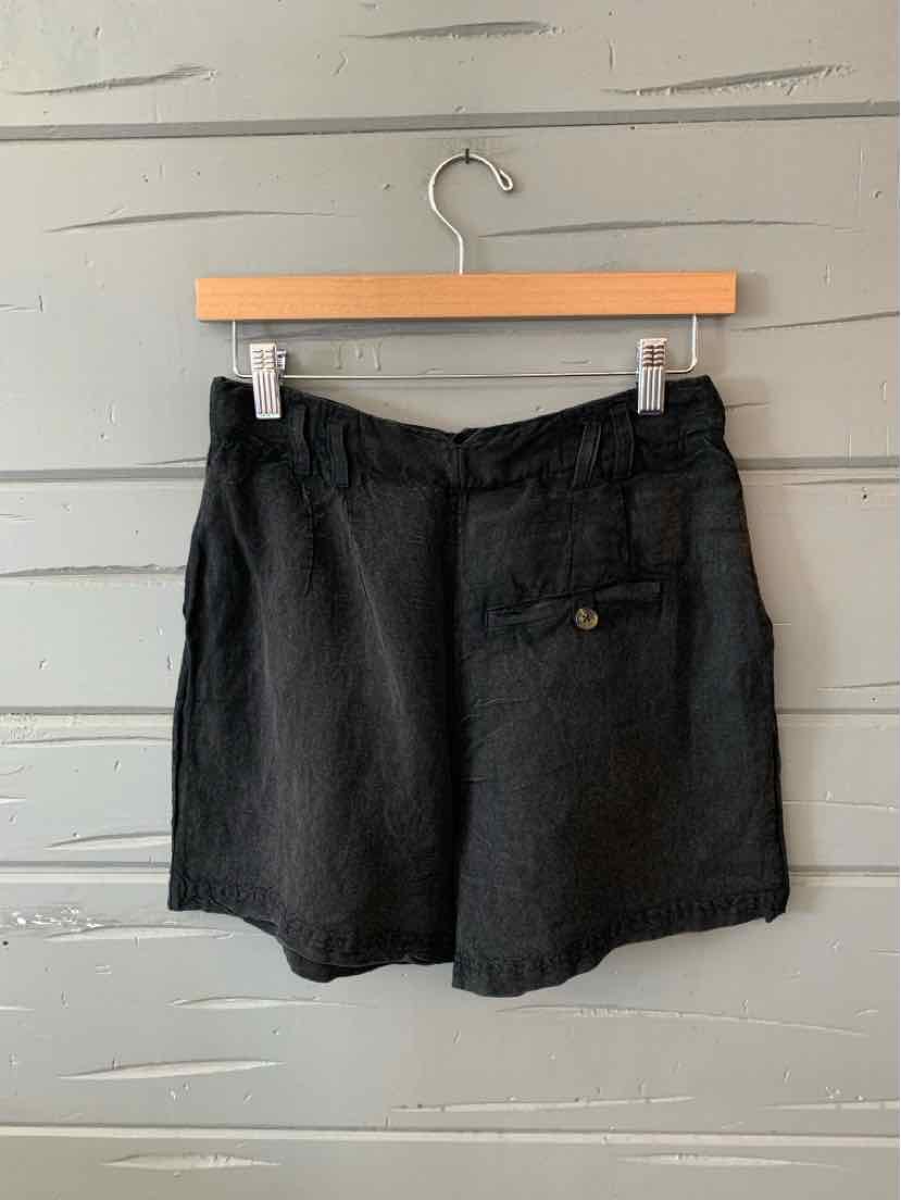 Black high-waisted shorts with a buttoned back pocket and belt loops hanging on wooden hanger.