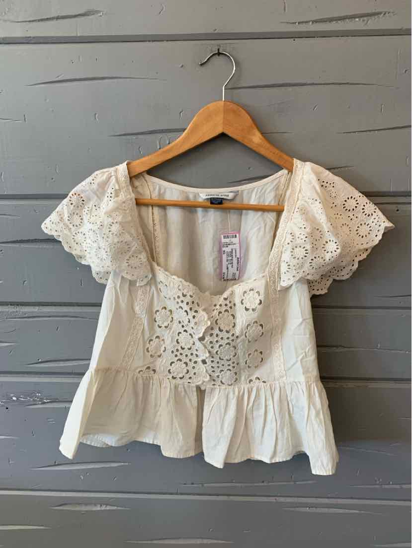 Beige eyelet lace blouse with short flutter sleeves and square neckline on wooden hanger.