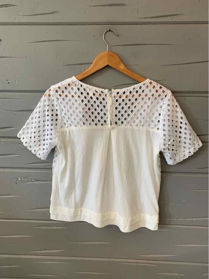 White short-sleeve blouse with perforated upper yoke and solid lower body on wooden hanger.