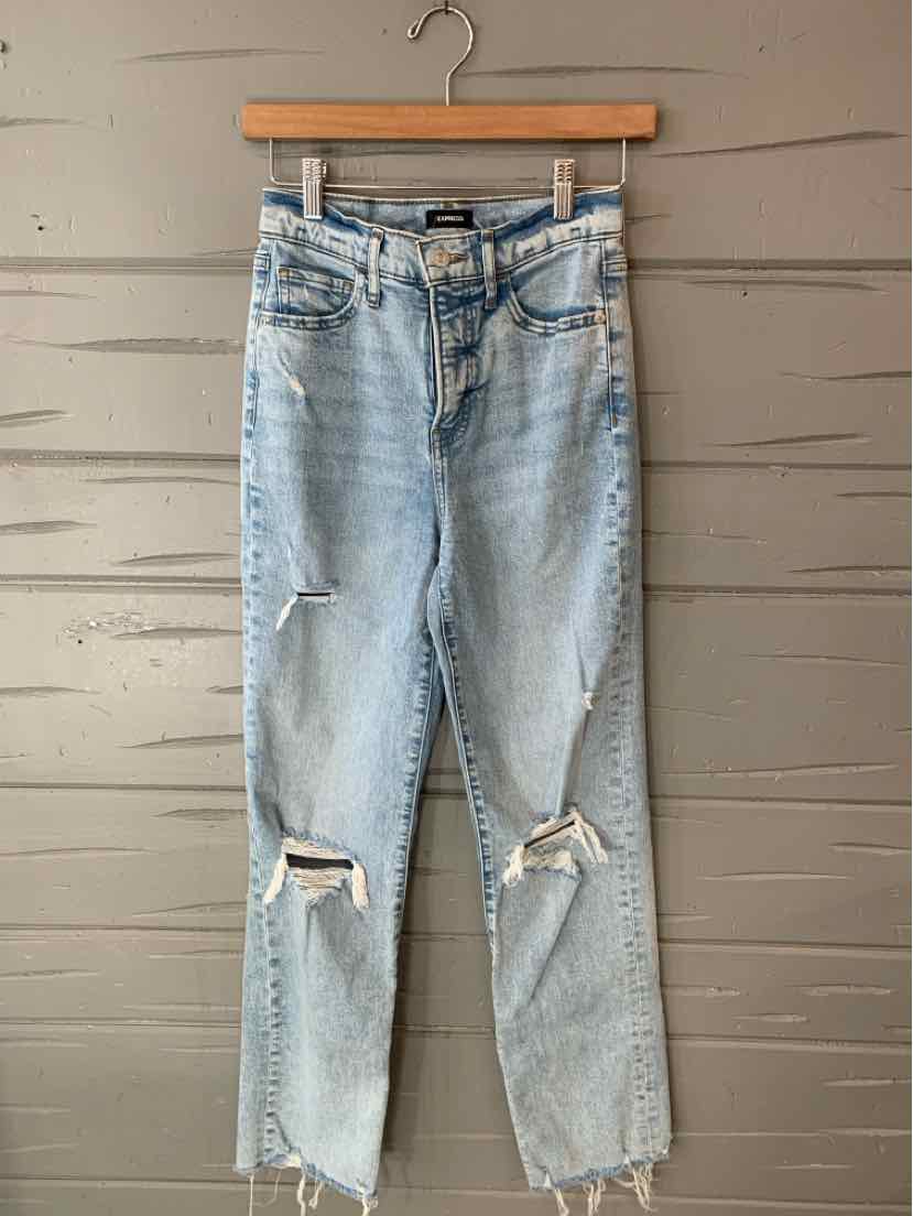 Light blue distressed denim jeans with ripped knees and classic five-pocket design hanging on wooden hanger.