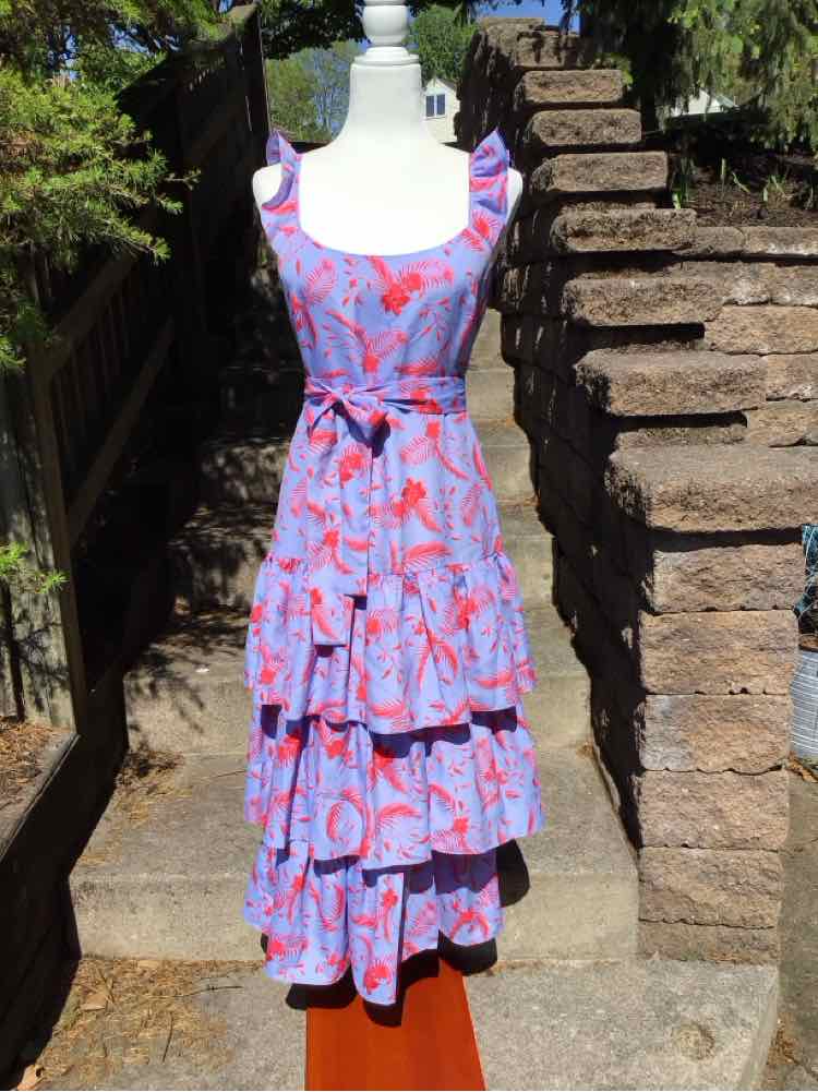 Sleeveless purple dress with red floral print and tiered ruffle skirt on mannequin outdoors.