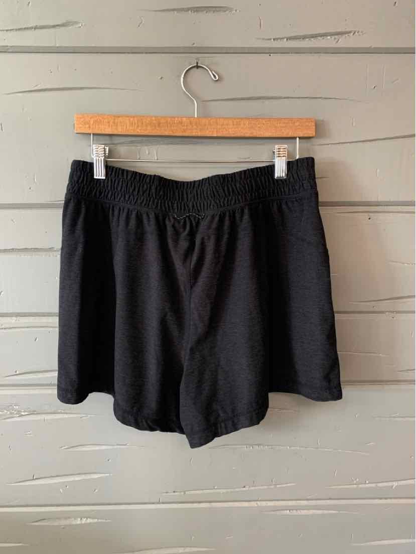 Black mid-length shorts with elastic waistband, soft fabric, and relaxed fit hanging on wooden hanger.