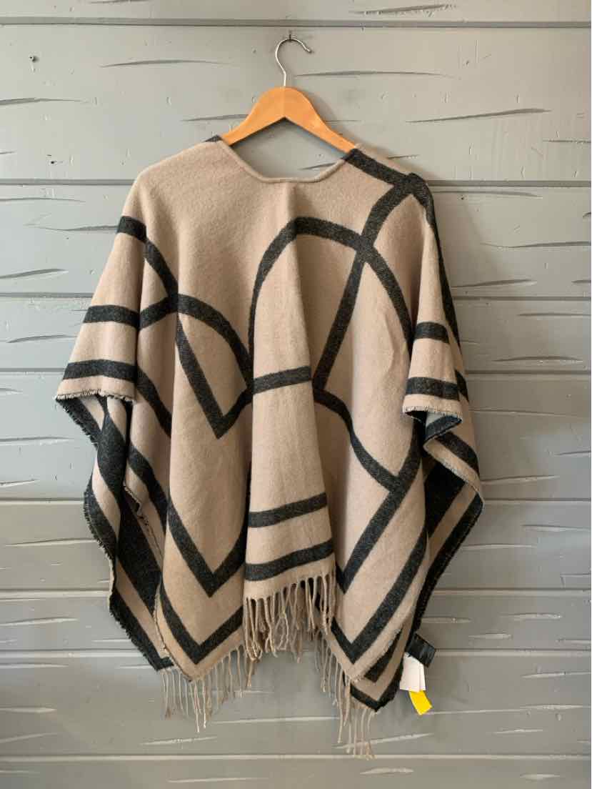 Beige knit poncho with black geometric lines and fringe trim hanging on wooden hanger.