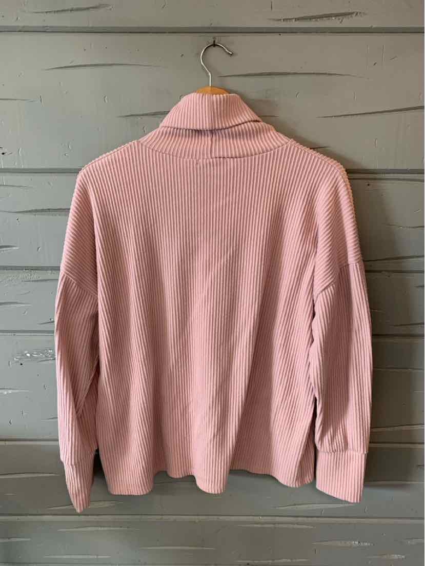 Light pink ribbed long-sleeve turtleneck sweater with a relaxed fit hanging on a wooden hanger.
