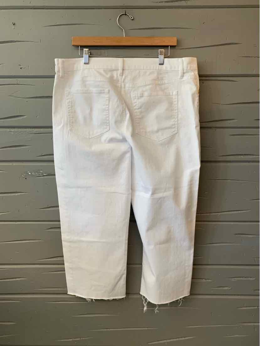 White straight-leg pants with back pockets and raw hem detail hanging on wooden hanger against gray wooden wall.