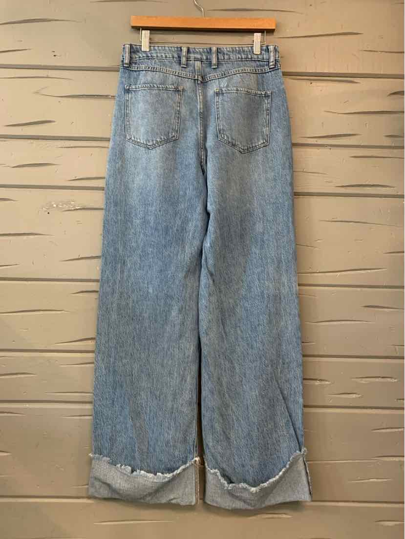Light-wash blue denim jeans with a relaxed straight-leg fit and folded cuffs, hanging from a wooden clip hanger.