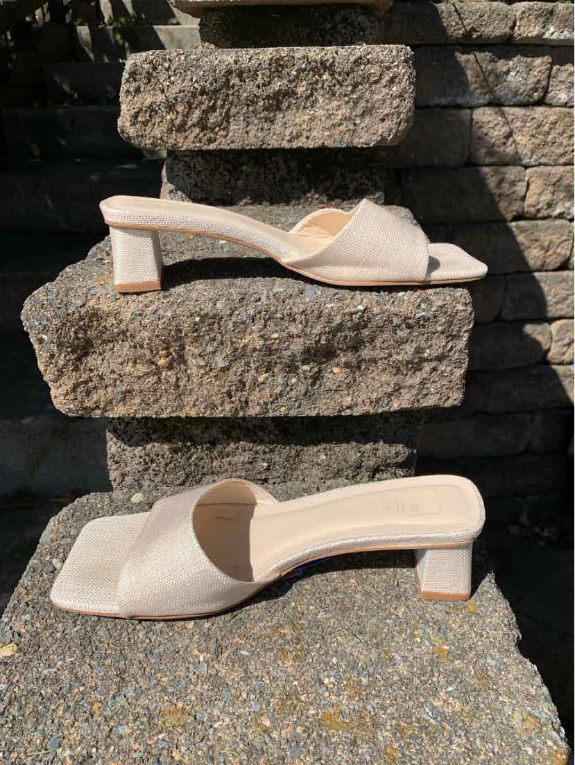 Beige open-toe mule sandals with low block heels and crisscross straps on stone steps.